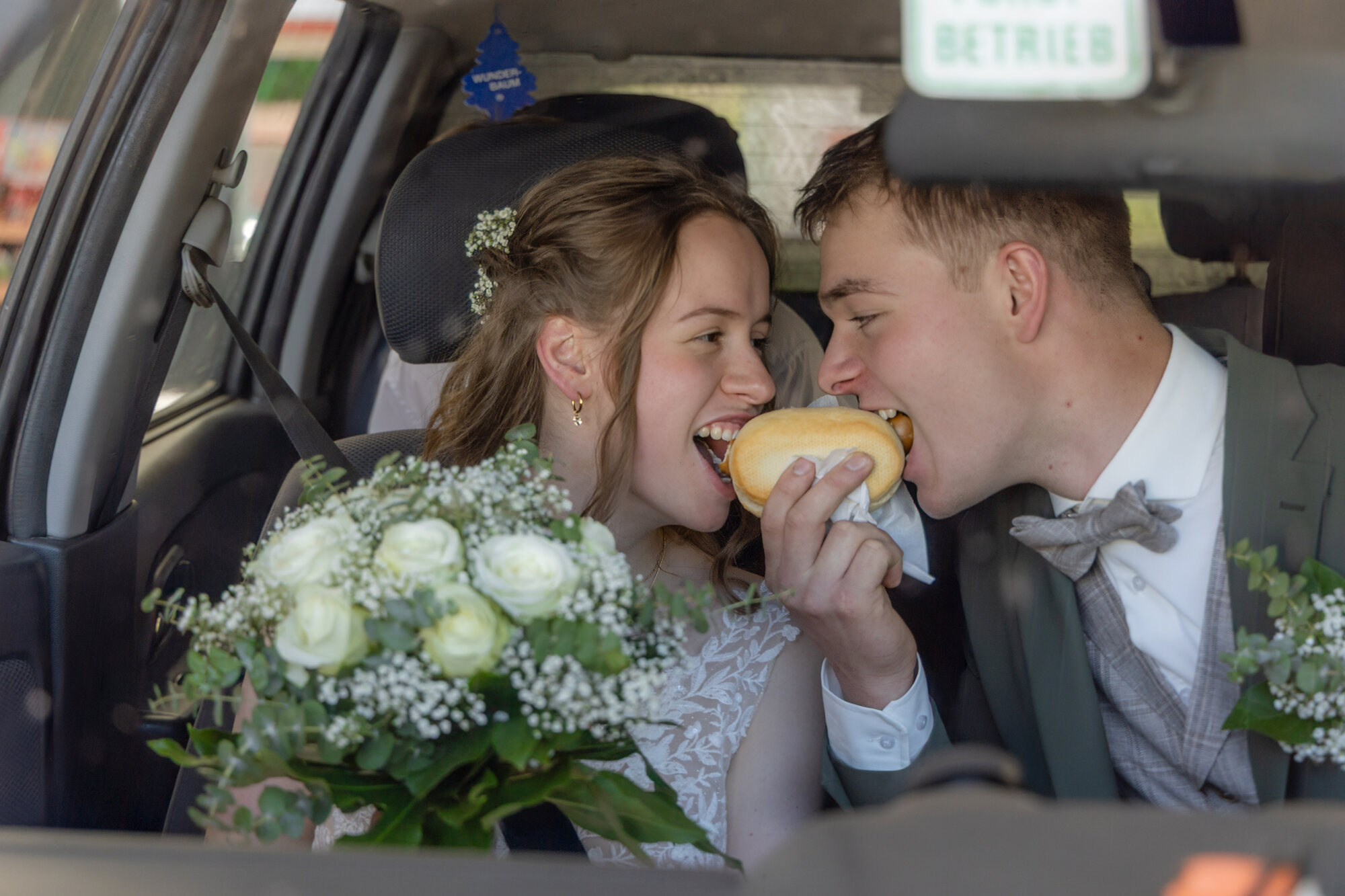 Brautpaar beißt im Hochzeitsauto gemeinsam in einen Krapfen – Hochzeitsfotograf Marko Lorenz