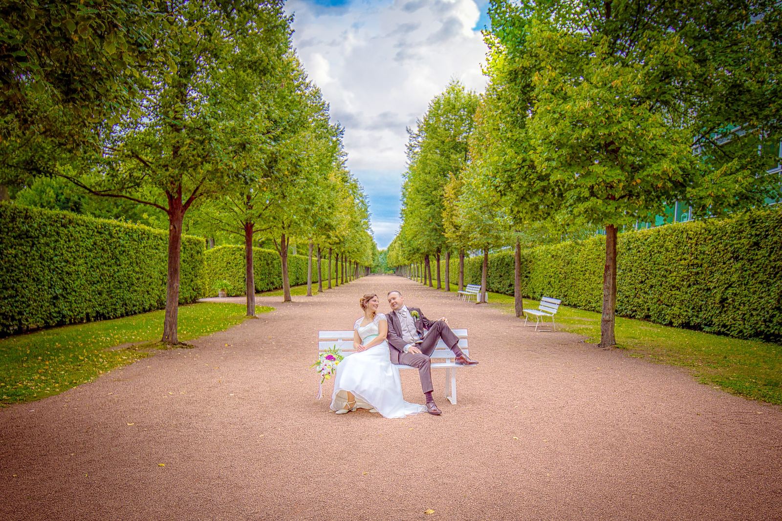 Brautpaar auf einer Bank in einer Allee – Marko Lorenz, Hochzeitsfotograf